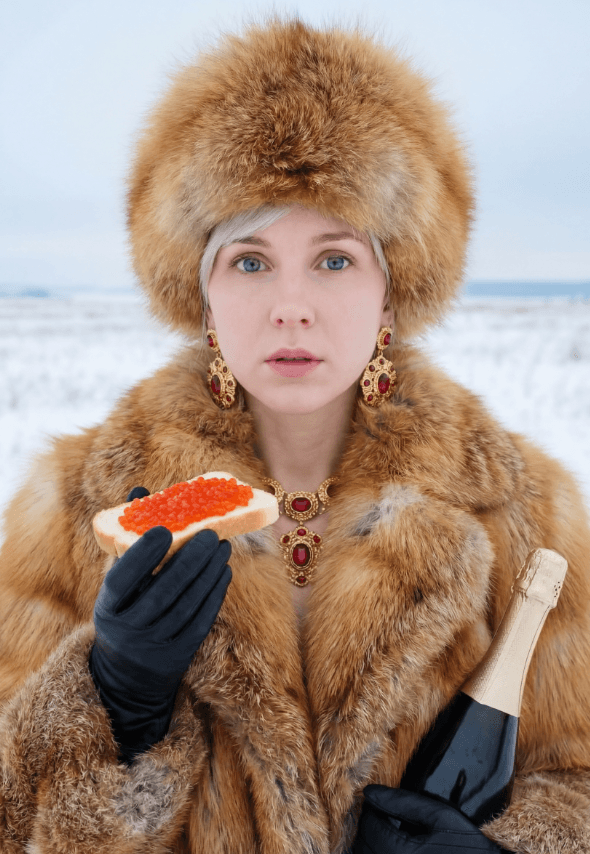 Человек в меховой шубе держит тост с красной икрой и бутылку шампанского на снегу